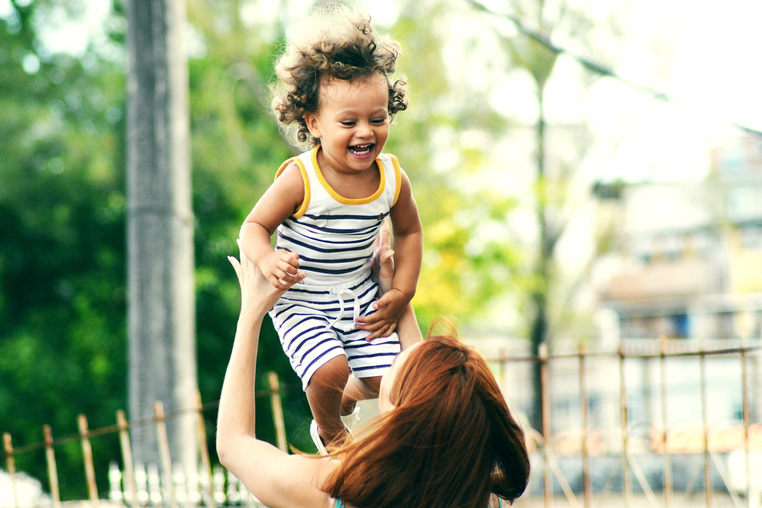 mum throwing toddler son in air at park